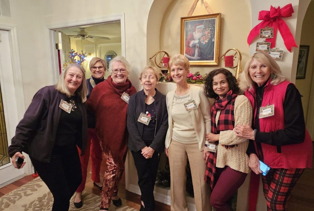 Seven women posing in a decorated room with festive holiday attire and name tags.