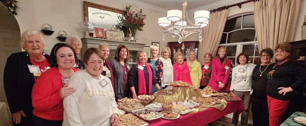 A group of people gathered around a table filled with assorted desserts in a festive room.