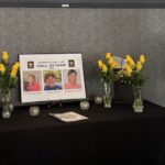 A woman stands next to a display table with yellow roses, candles, and a "Women's Club Hall of Fame" sign featuring three women's photos.